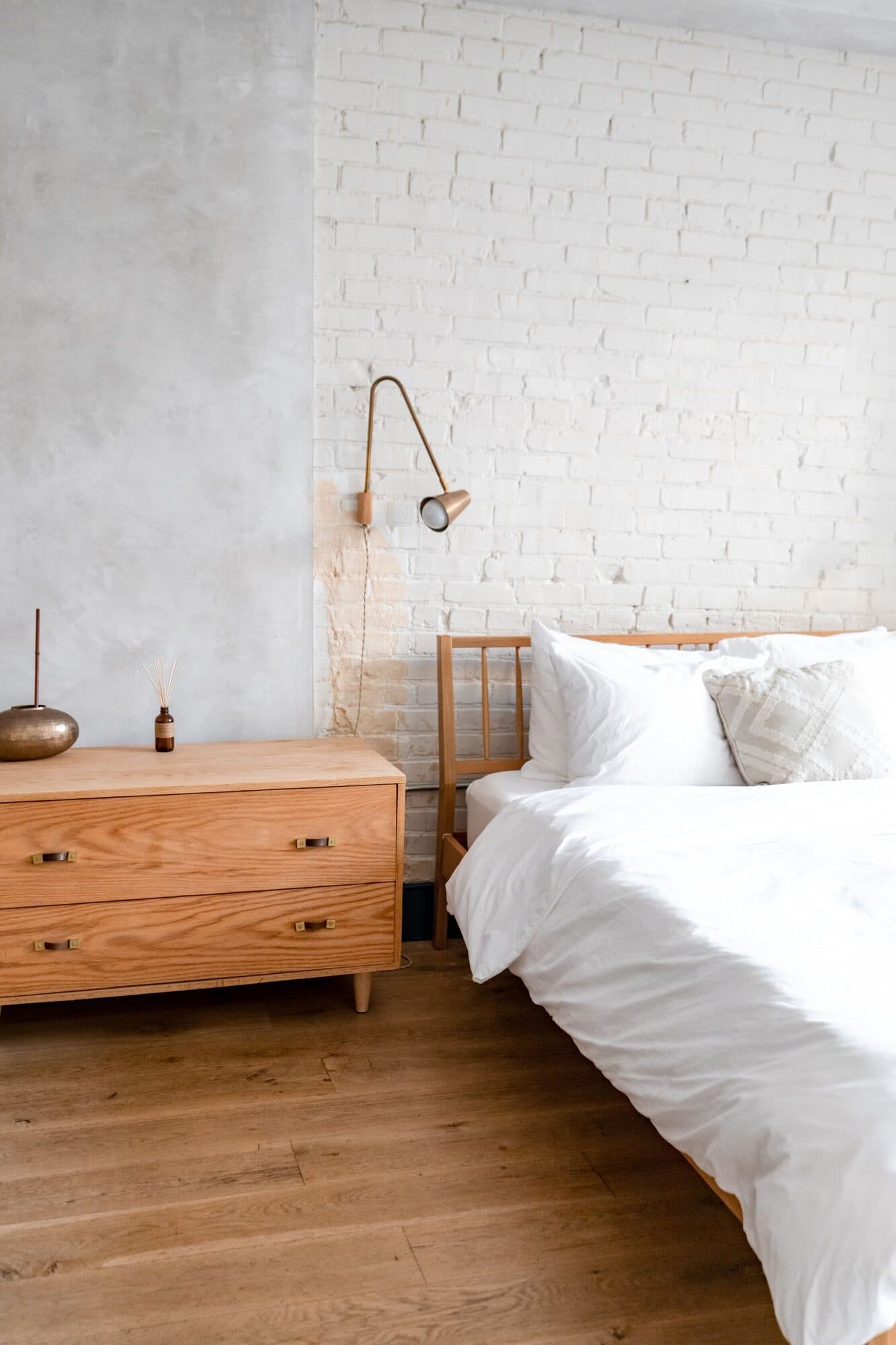 Una camera da letto ordinata e luminosa, con il letto rifatto e toni chiari di legno e bianco